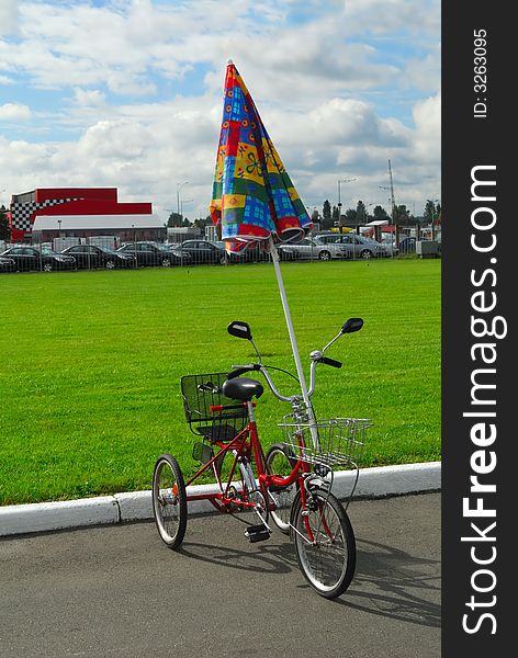 Tricycle with umbrella and car parking on background