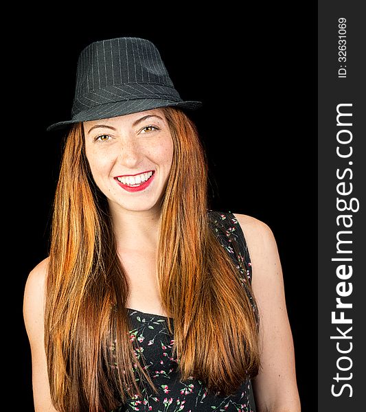 Happy smiling young woman with long red hair and hazel eyes wearing a pinstriped fedora isoaled on black