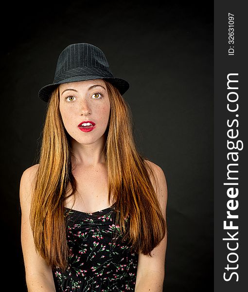 Very cute girl with red hair freckles and beautiful hazel eyes wearing a pinstriped fedora against a dark background. Very cute girl with red hair freckles and beautiful hazel eyes wearing a pinstriped fedora against a dark background
