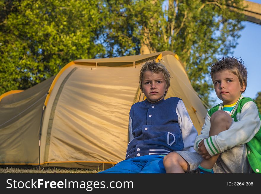 Two boys sitting in front of a tent, looking at the sunset. Two boys sitting in front of a tent, looking at the sunset