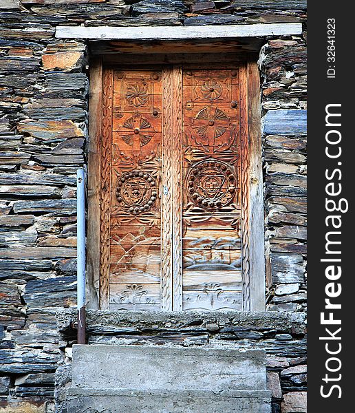 Vintage wooden door with ornament on stone wall background. Georgia