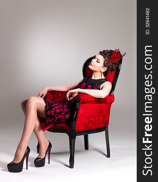 Beautiful adult woman with fashion hairstyle and red armchair poses at studio
