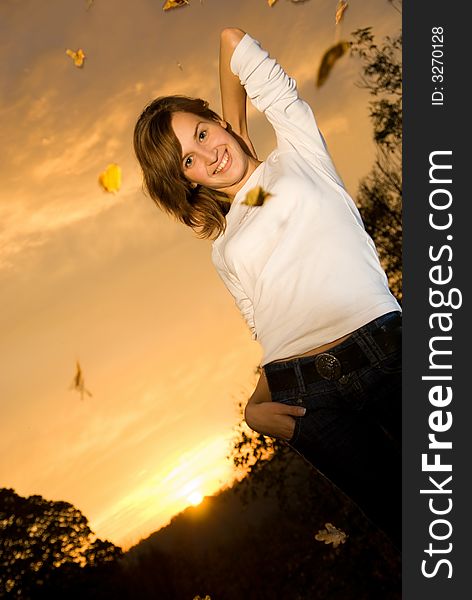 Beautiful young girl at sunset time and falling autumn leaves around her