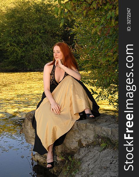 Auburn haired woman sits by lake. Auburn haired woman sits by lake.