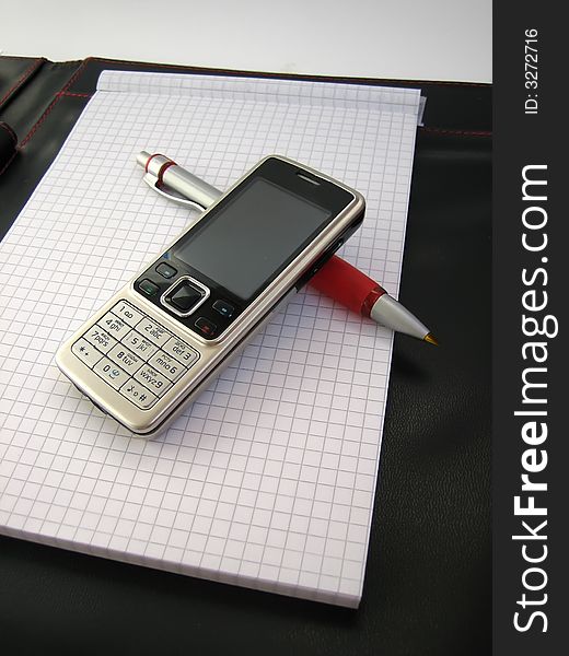 Mobile phone with pen are on business notepad. Mobile phone with pen are on business notepad.
