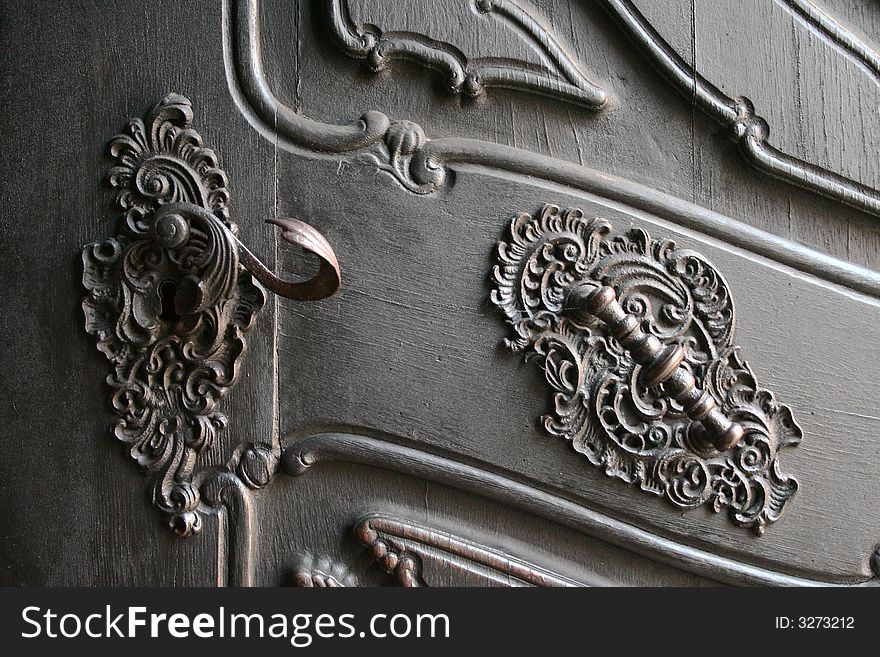 A detail of a large antique door handle and pull mounted in beautiful ironwork. A detail of a large antique door handle and pull mounted in beautiful ironwork.