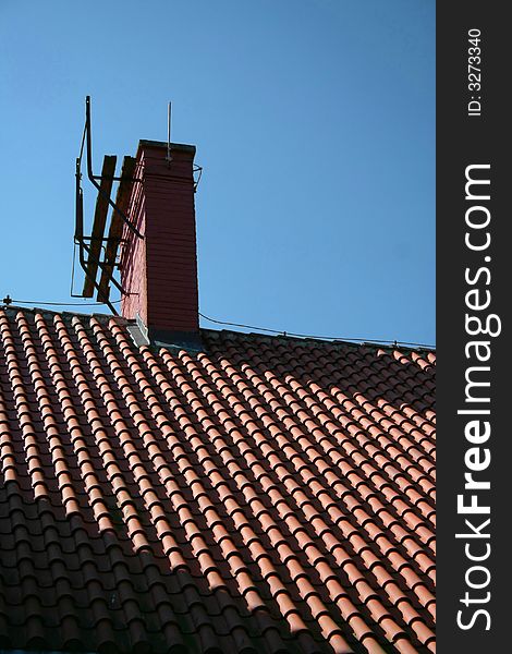 A chimney on top of a newly tiled roof on a bright summer day (deep shadows, red roof, blue sky).