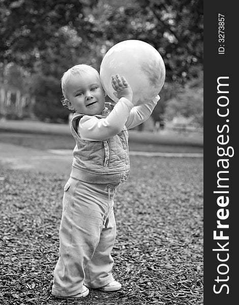 Black and white image of a small caucasian blond toddler holding an inflated rubber ball in a park setting. Black and white image of a small caucasian blond toddler holding an inflated rubber ball in a park setting