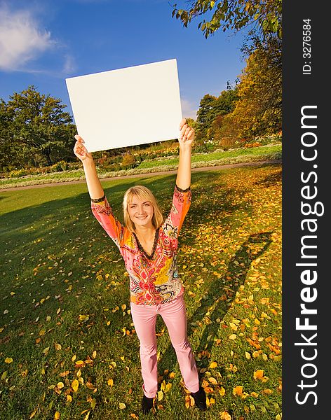Beautiful girl on autumn background holding a white noticeboard