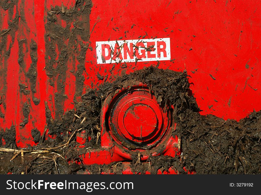 Danger sign splattered by muck on the back of a red muck spreader. Danger sign splattered by muck on the back of a red muck spreader