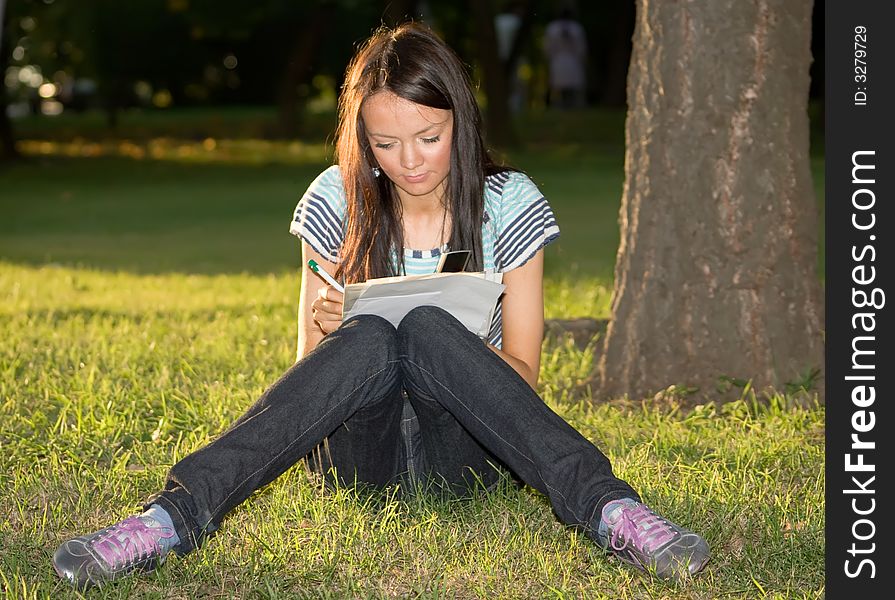 Girl sits on a green grass and writes on a paper. Girl sits on a green grass and writes on a paper