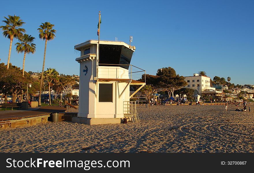 The image shows the iconic lifeguard tower on the main beach of Laguna Beach, California. The white building in the background is the historic Hotel Laguna built in 1930. The lifeguard tower was once an office for a gas station on Coast Highway in the early days of Laguna Beach. The image shows the iconic lifeguard tower on the main beach of Laguna Beach, California. The white building in the background is the historic Hotel Laguna built in 1930. The lifeguard tower was once an office for a gas station on Coast Highway in the early days of Laguna Beach.