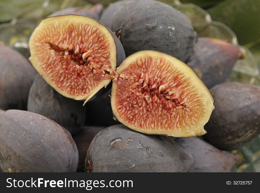 A pair of cut plump ripe mission figs on top of a harvest of more figs with a glass dish visible. A pair of cut plump ripe mission figs on top of a harvest of more figs with a glass dish visible