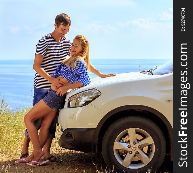 Young man and woman in stand at car against sea