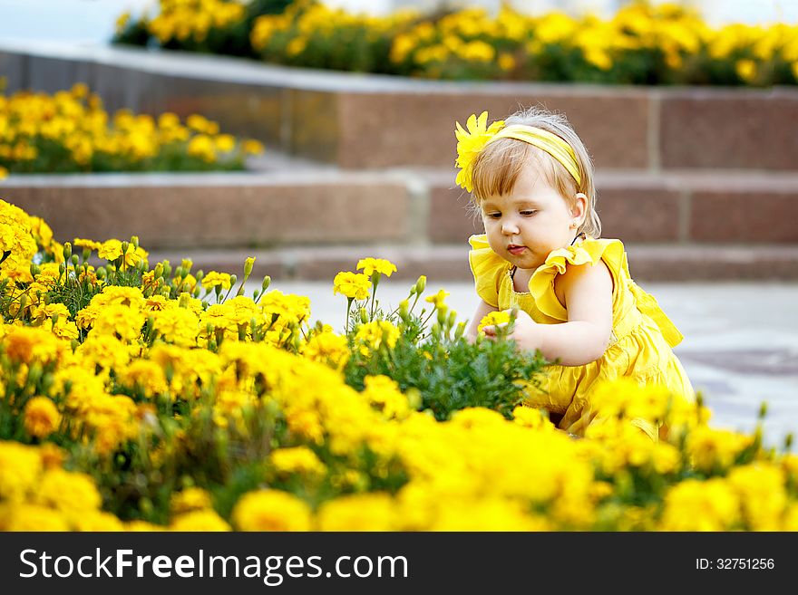 Girl in a yellow dress sits near a flower bed with yellow flowers. Girl in a yellow dress sits near a flower bed with yellow flowers