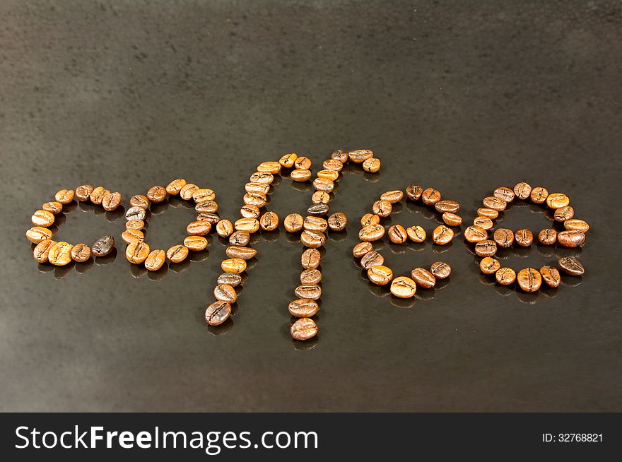 The photograph shows coffee beans on a black background, they form an inscription that reads coffee. The photograph shows coffee beans on a black background, they form an inscription that reads coffee.