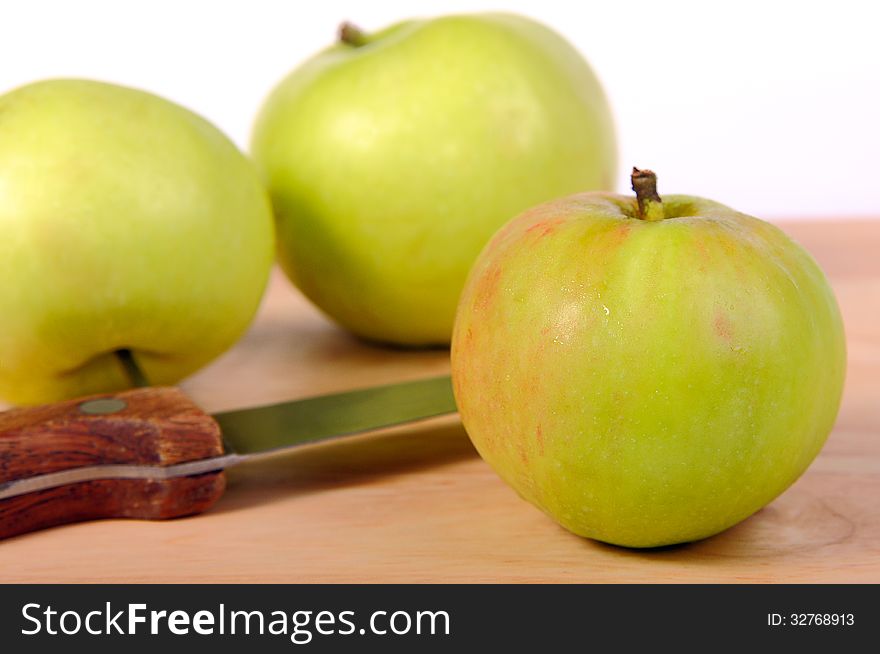 Several green apples and knife on a wooden board