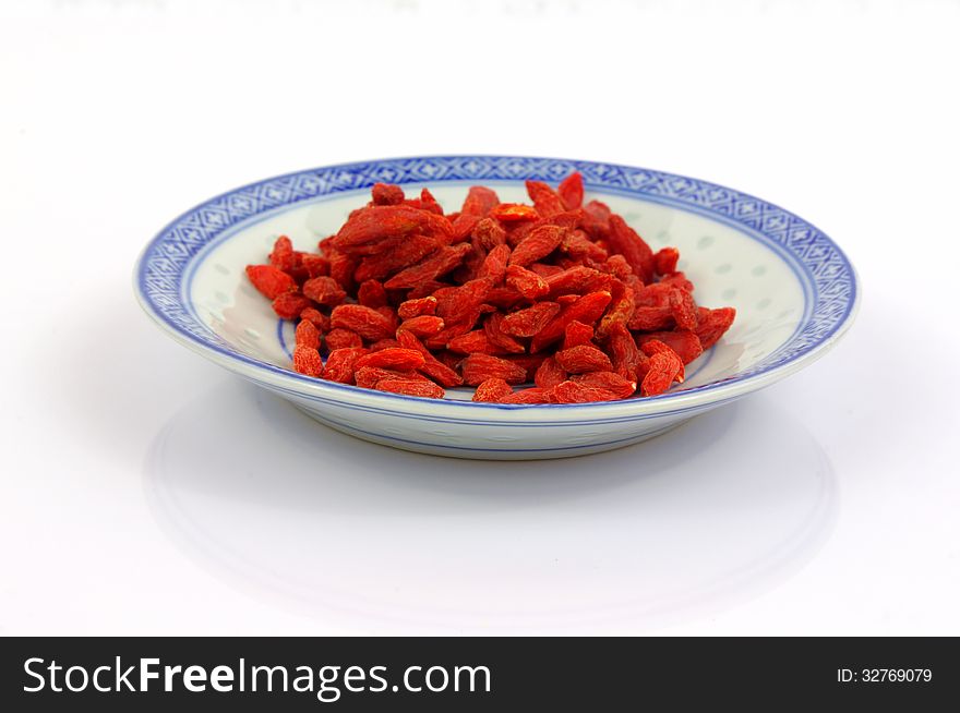 The photograph shows the goji berry placed on a porcelain saucer placed on a white background. The photograph shows the goji berry placed on a porcelain saucer placed on a white background.