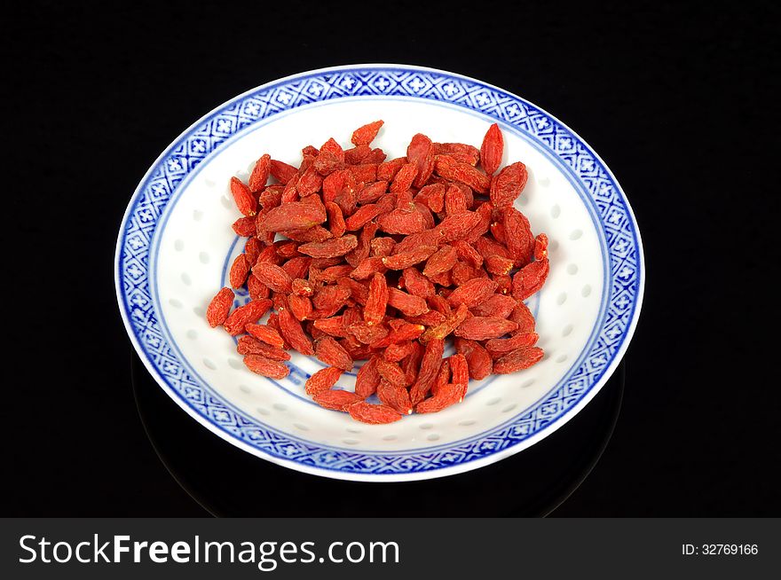 The photograph shows the goji berry placed on a porcelain saucer placed on a black mirrored background. The photograph shows the goji berry placed on a porcelain saucer placed on a black mirrored background.