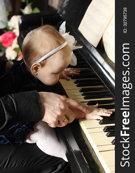 Cute baby sits at knees of father and plays piano