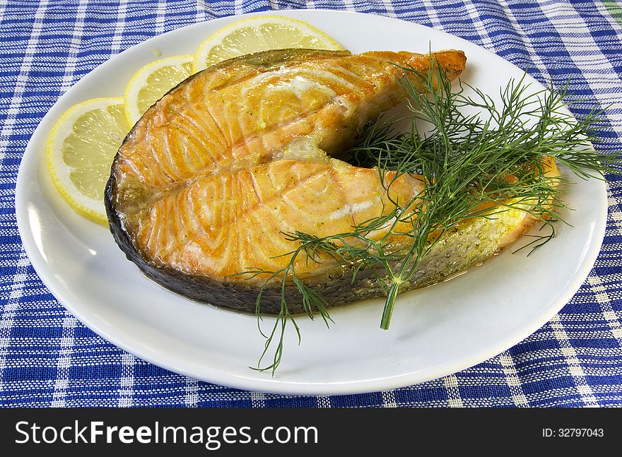 Fried salmon on a plate with lemon and dill on a blue checkered table cloth