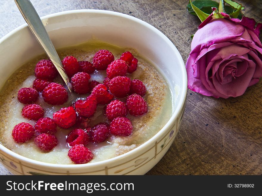 Bowl of porridge with applesauce and fresh raspberries and a rose on the table beside the bowl. Bowl of porridge with applesauce and fresh raspberries and a rose on the table beside the bowl.