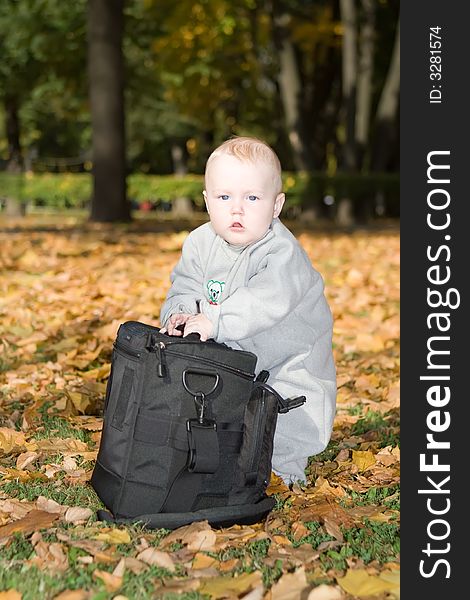 Little child stands on the yellow fallen foliage near to the big black bag. Little child stands on the yellow fallen foliage near to the big black bag