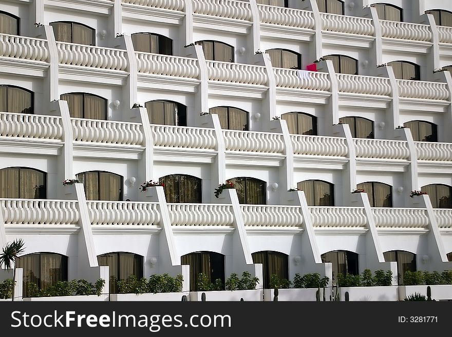 This is a detailed view of a great hotel by the sea on Teneriffa. White balconies with one magenta beach mattress.