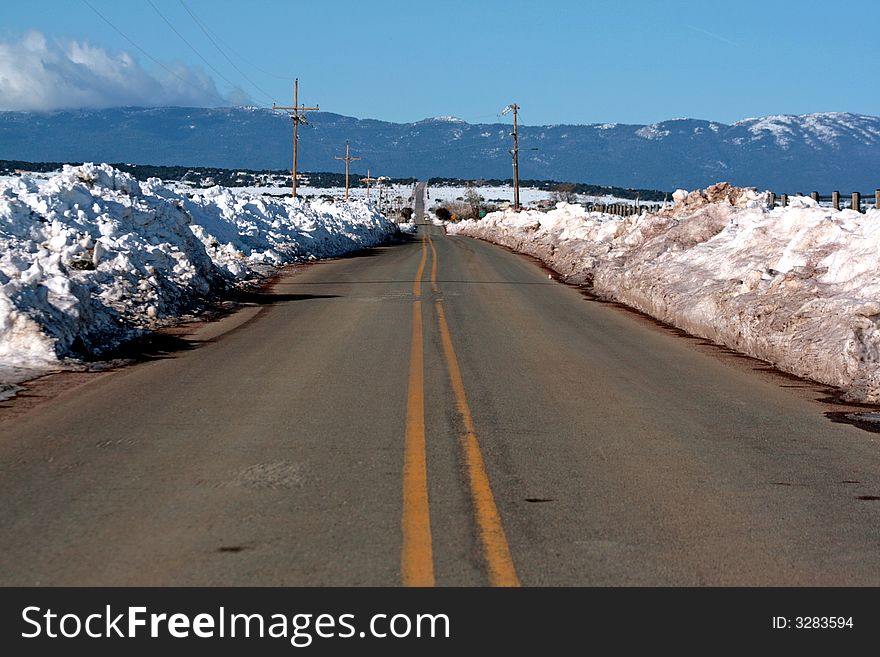 A long rural road wanes off in the distance toward mountains, heaps of newly plowed snow on both shoulders. A long rural road wanes off in the distance toward mountains, heaps of newly plowed snow on both shoulders.