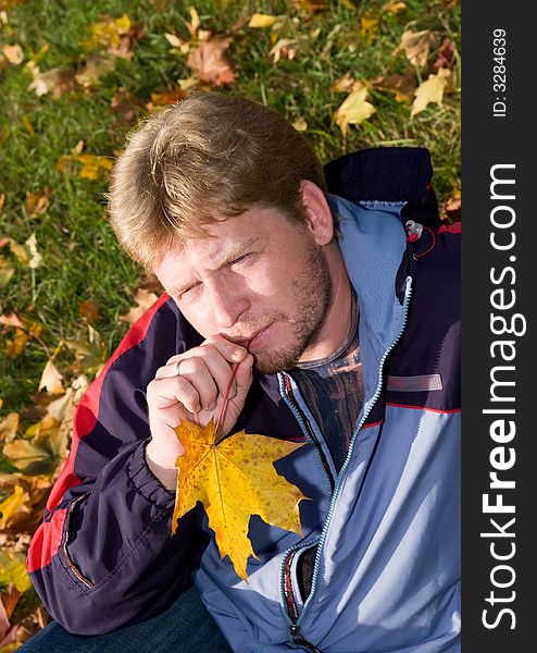 The man sits on a grass with yellow leaves. The man sits on a grass with yellow leaves.