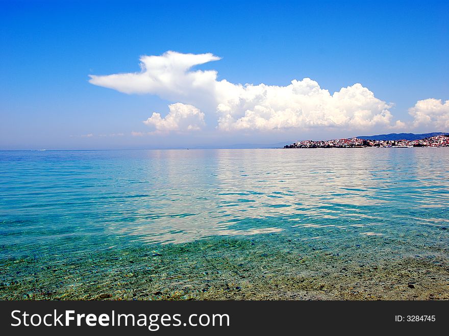 Seaside sandy beach distant greek fishing village clouds. Seaside sandy beach distant greek fishing village clouds
