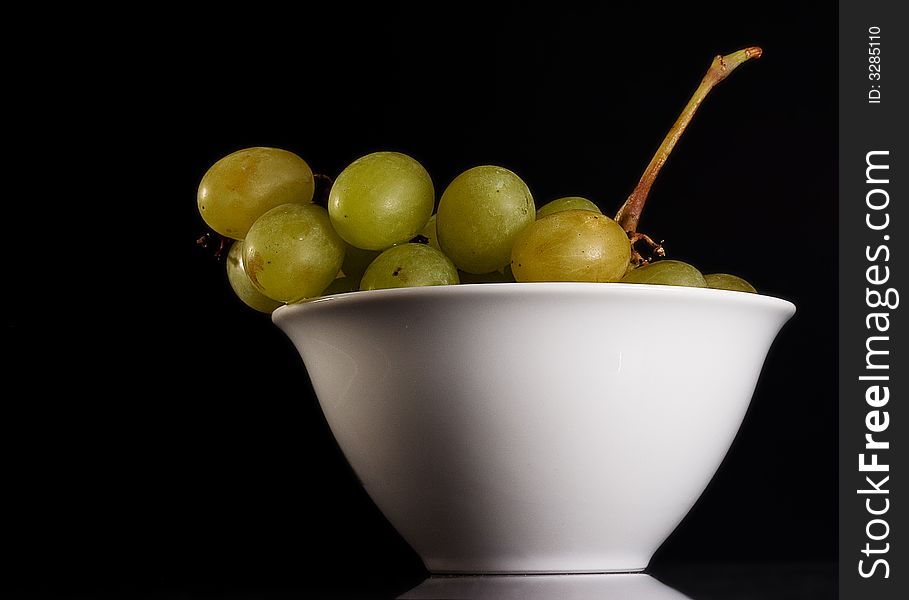 Withe grapes into a withe bowl against a black background