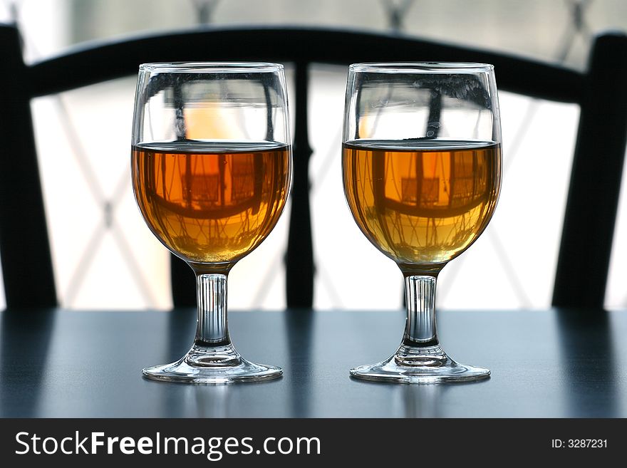 Two glasses of tea on a black table top with outdoor natural light behind