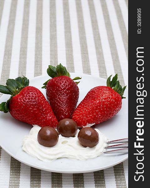 Three strawberries with chocolate balls lying in cream on white saucer. Three strawberries with chocolate balls lying in cream on white saucer