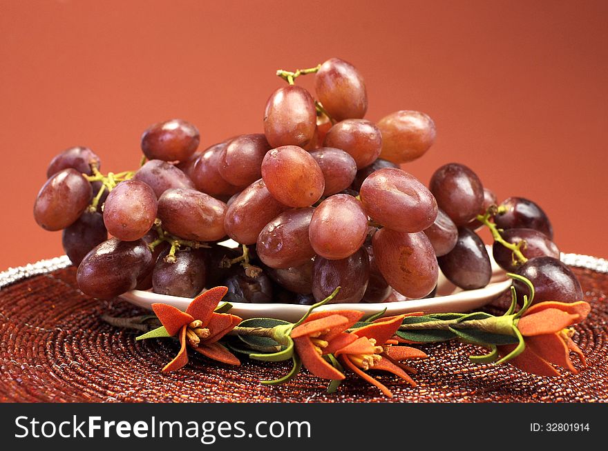 Plate of healthy fruit, red grapes, in red brown autumn fall setting with flowers.