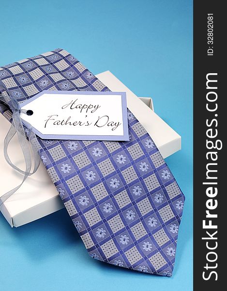 Happy Fathers Day gift of a blue pattern check tie in a white gift box present with gift tag against a blue background. Vertical. Happy Fathers Day gift of a blue pattern check tie in a white gift box present with gift tag against a blue background. Vertical.