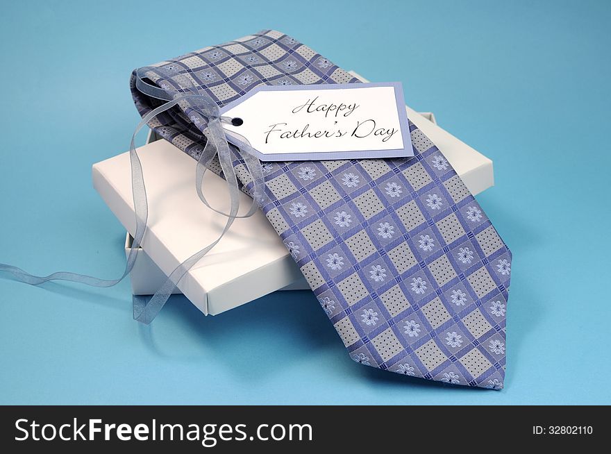 Happy Fathers Day gift of a blue pattern check tie in a white gift box present with gift tag against a blue background.