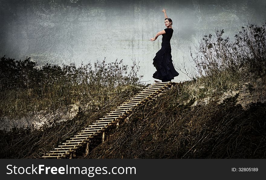 Enigmatic woman in black dancing in the dunes, on the top of the stairs