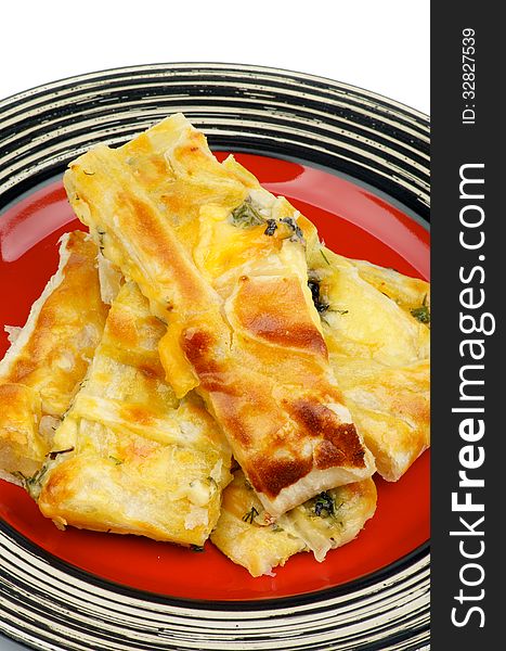 Pile of Cheese and Greens Puff Pastry Pie on Red Striped Plate closeup on white background. Pile of Cheese and Greens Puff Pastry Pie on Red Striped Plate closeup on white background