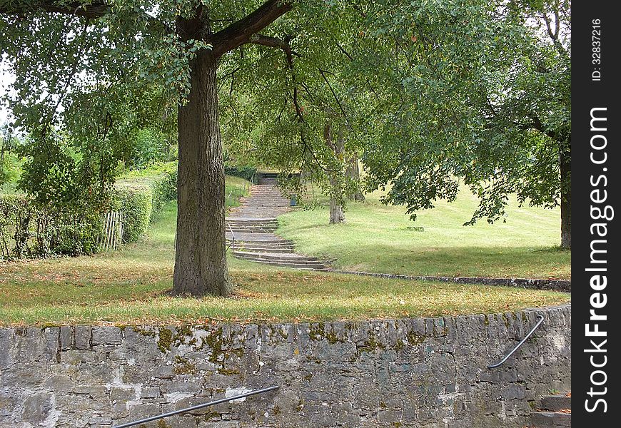 A big oak in the park casts shade on a flight of stone stairs and a path. A big oak in the park casts shade on a flight of stone stairs and a path