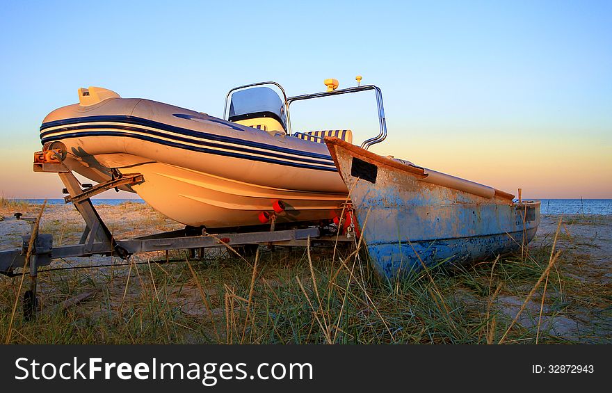 Two old and new boats hauled up abreast  near the beach at dusk. Two old and new boats hauled up abreast  near the beach at dusk