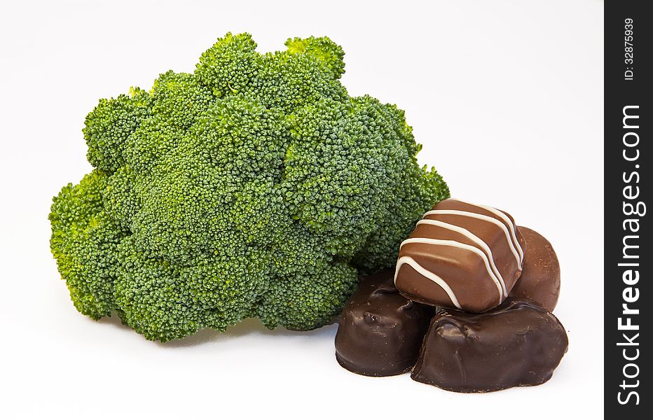 Raw green broccoli and four chocolate candies against a white background. Raw green broccoli and four chocolate candies against a white background