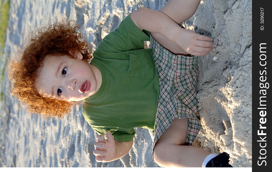 A curly red haired todder on the beach. A curly red haired todder on the beach