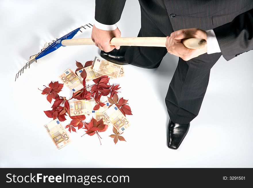 The businessman rakes up autumn leaves together with money. The businessman rakes up autumn leaves together with money