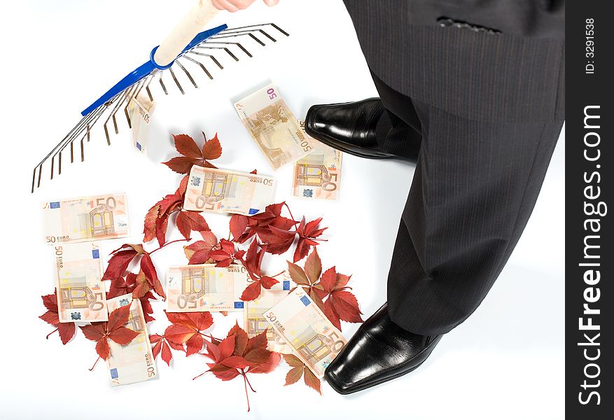 The businessman rakes up autumn leaves together with money. The businessman rakes up autumn leaves together with money
