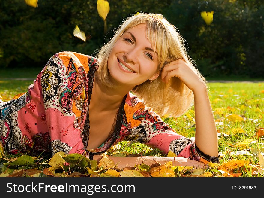 Blond cheerful girl lying on autumn leaves