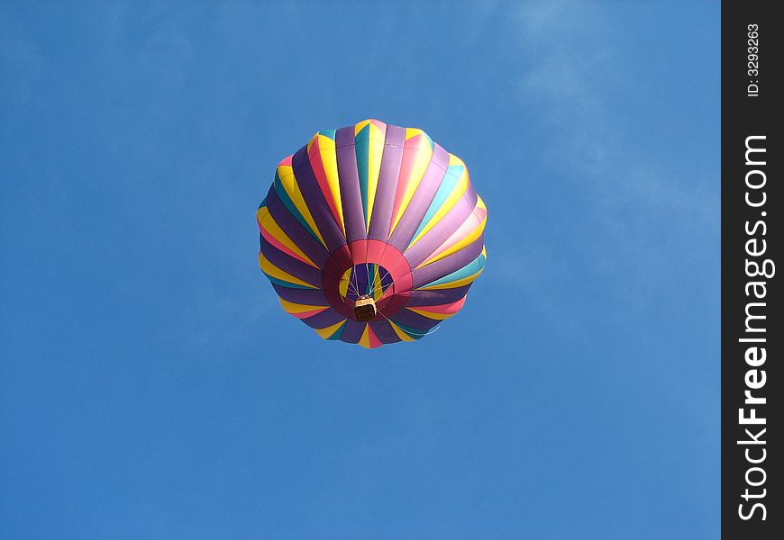 Hot air balloon flying across blue sky multiple colors