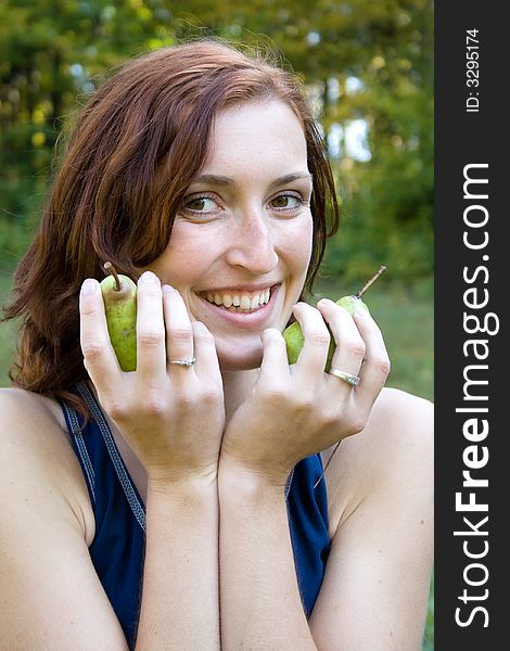 A smiling woman is holding pears in green nature