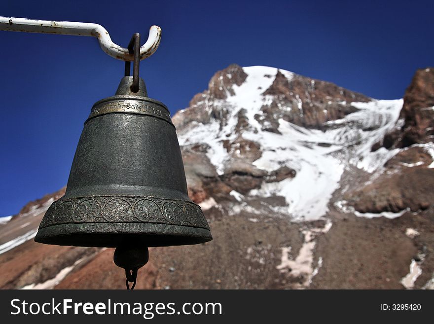 An old, Georgian bell hanging on the hook with the Kazbek mountain in the background. An old, Georgian bell hanging on the hook with the Kazbek mountain in the background.