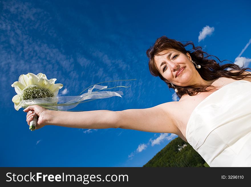 Fancy Perspective. Bride holds her bridal bouquet on outstretched arm. Deepblue sky as background. Sunny weather. Adult bride. Fancy Perspective. Bride holds her bridal bouquet on outstretched arm. Deepblue sky as background. Sunny weather. Adult bride.